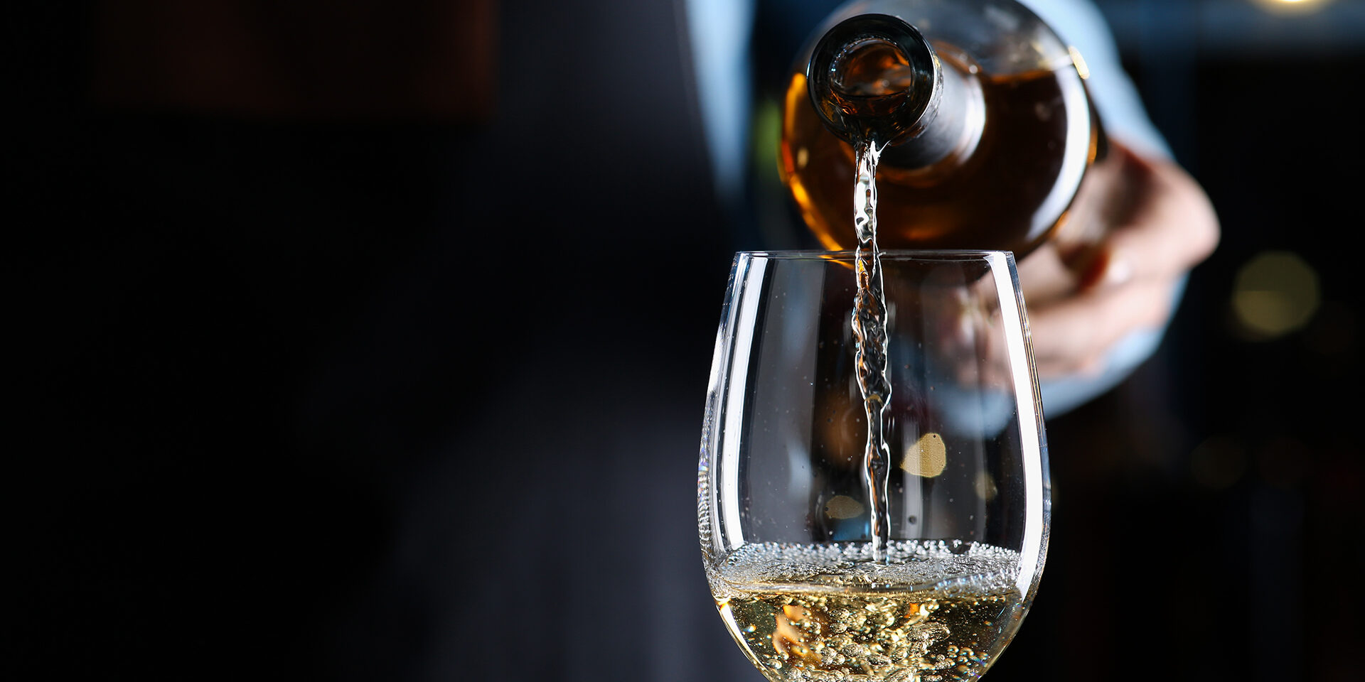 Bartender pouring white wine from bottle into glass indoors, closeup. Space for text Bartender pouring white wine from bottle into glass indoors, closeup. Space for text