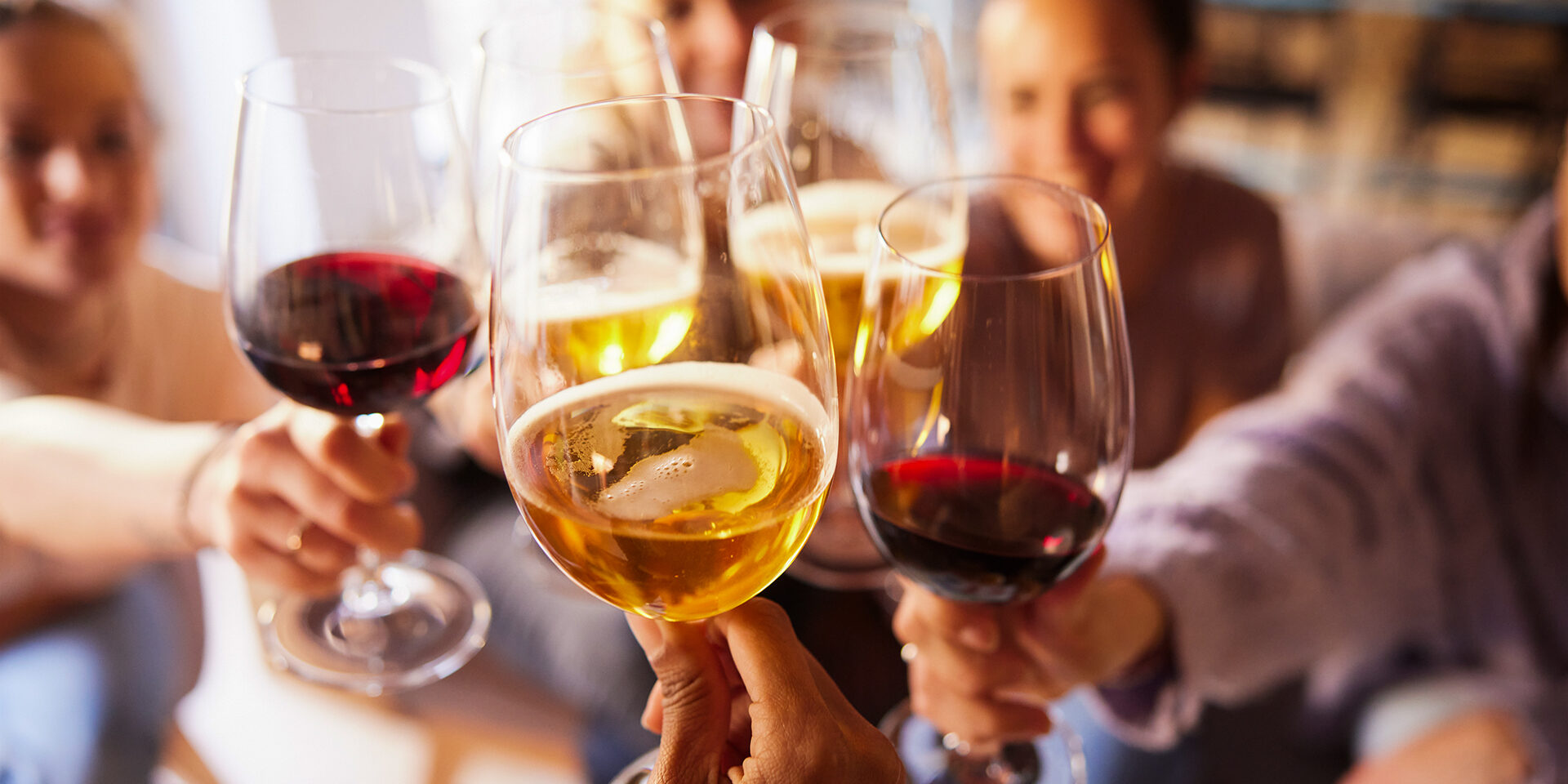 Close-up of wine and beer cups. Incidental people are making a toast.
