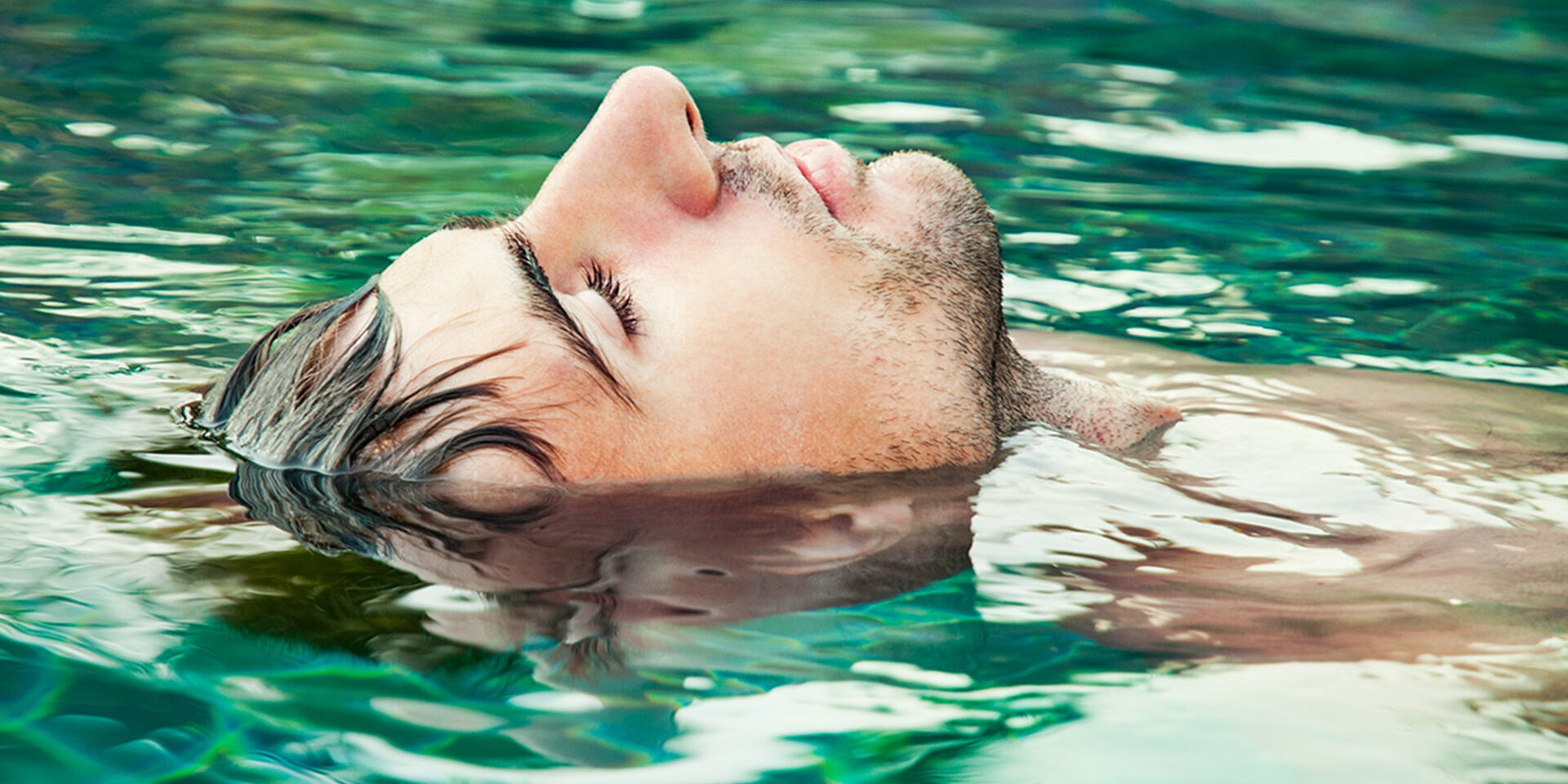 An image of a man with his eyes closed floating in water Portrait of a young man relaxing in the swimming pool
