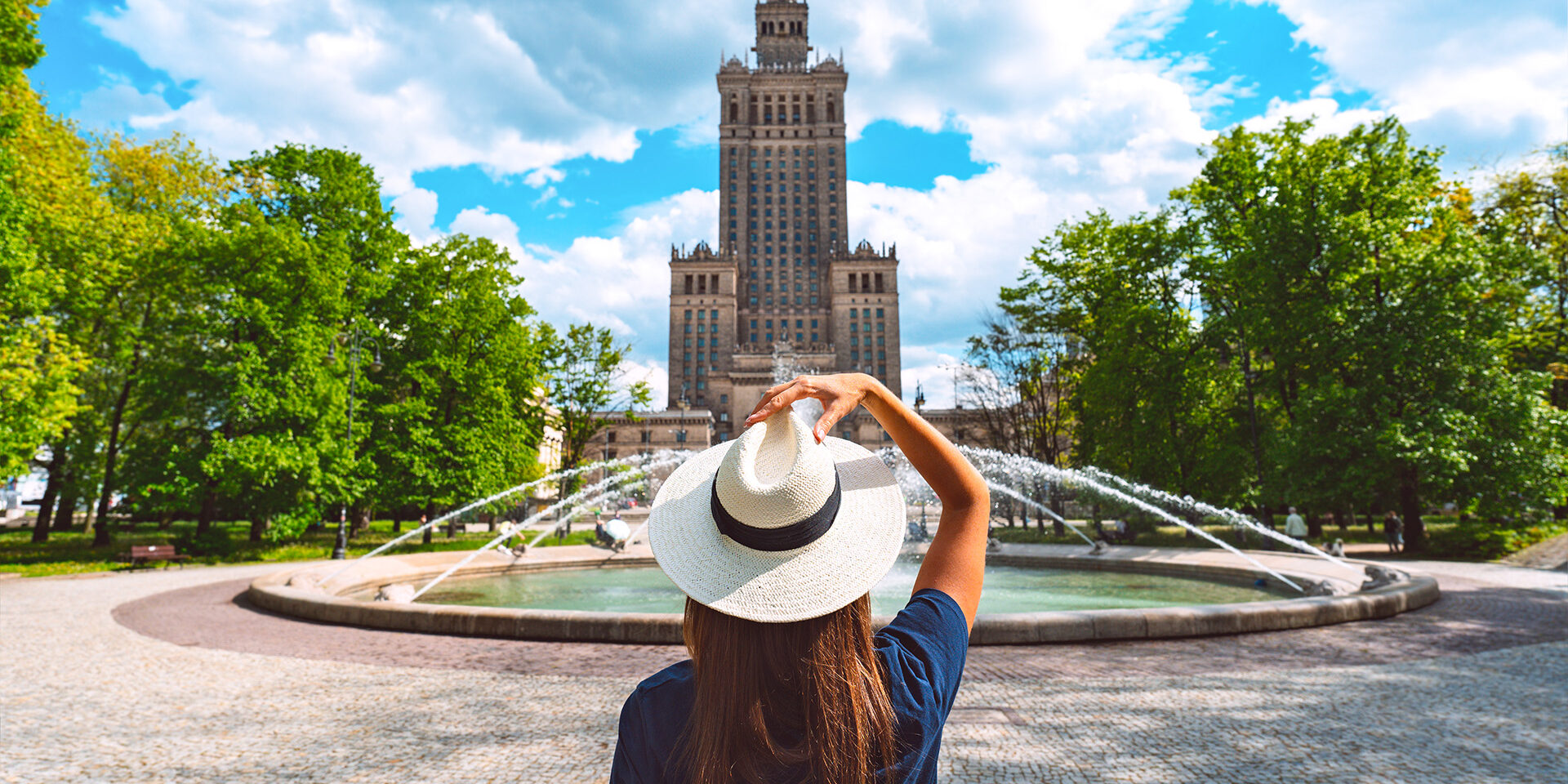 Young tourist woman in white sun hat walking in the park near Palace of Culture and Science in Warsaw city, Poland. Summer vacation in Warsaw. High quality photo