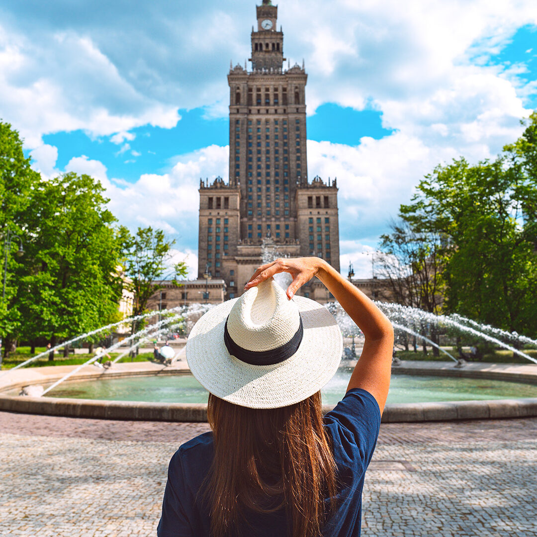 Young tourist woman in white sun hat walking in the park near Palace of Culture and Science in Warsaw city, Poland. Summer vacation in Warsaw. High quality photo