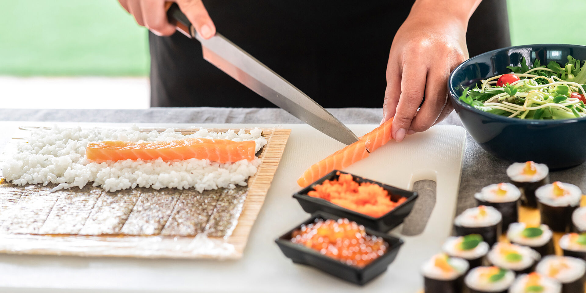 Chef preparing sushi. Chef preparing sushi. Asian woman chef in black uniform, cutting another piece of raw salmon to put on nori.