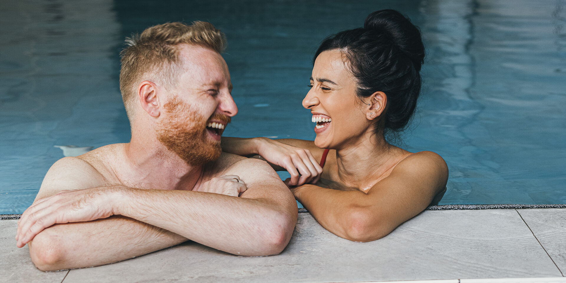 Smiling girlfriend and boyfriend in swimwear talking together in the swimming pool