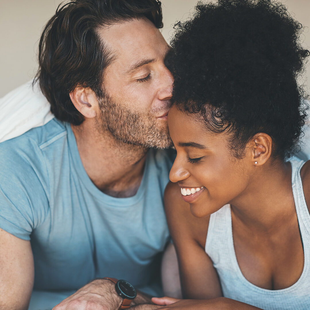 Shot of an affectionate middle aged man kissing his wife on her forehead while relaxing on their bed at home