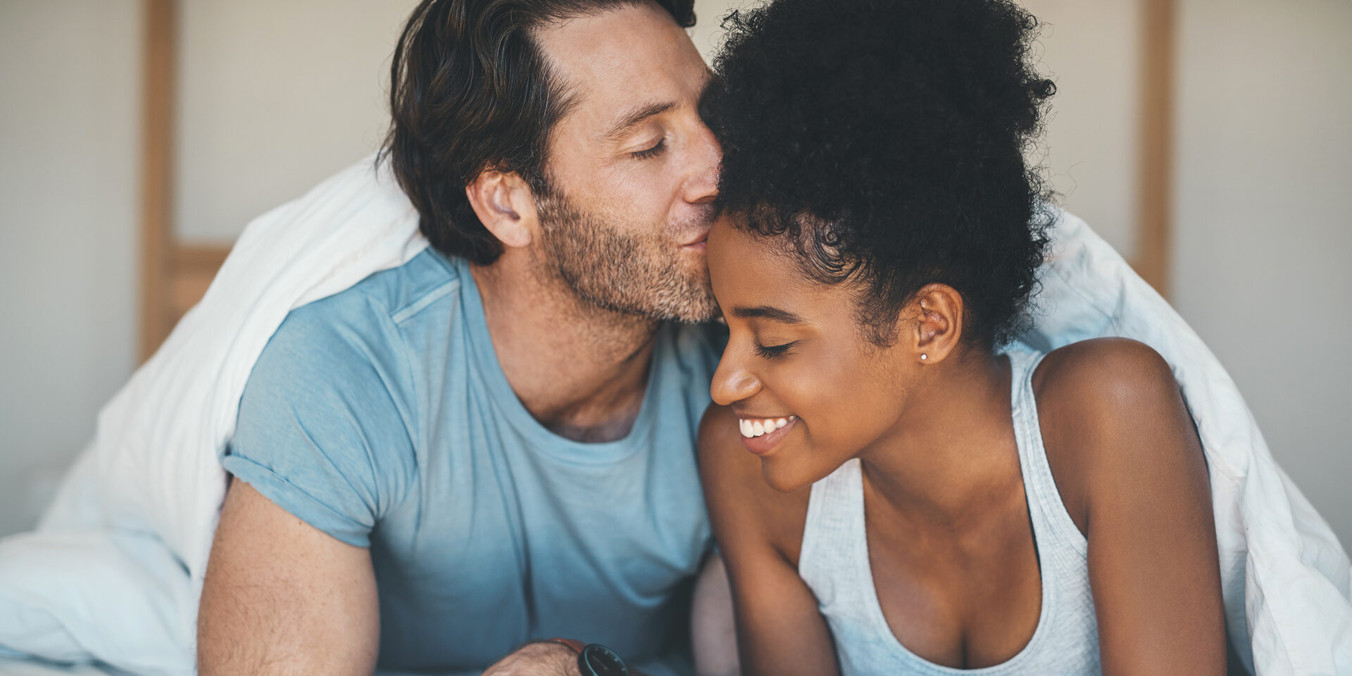 Shot of an affectionate middle aged man kissing his wife on her forehead while relaxing on their bed at home