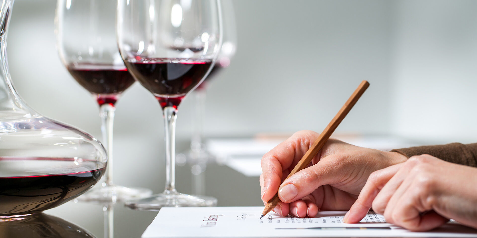 Female hand taking notes at red wine tasting. Extreme close up of female hand taking notes at red wine tasting.