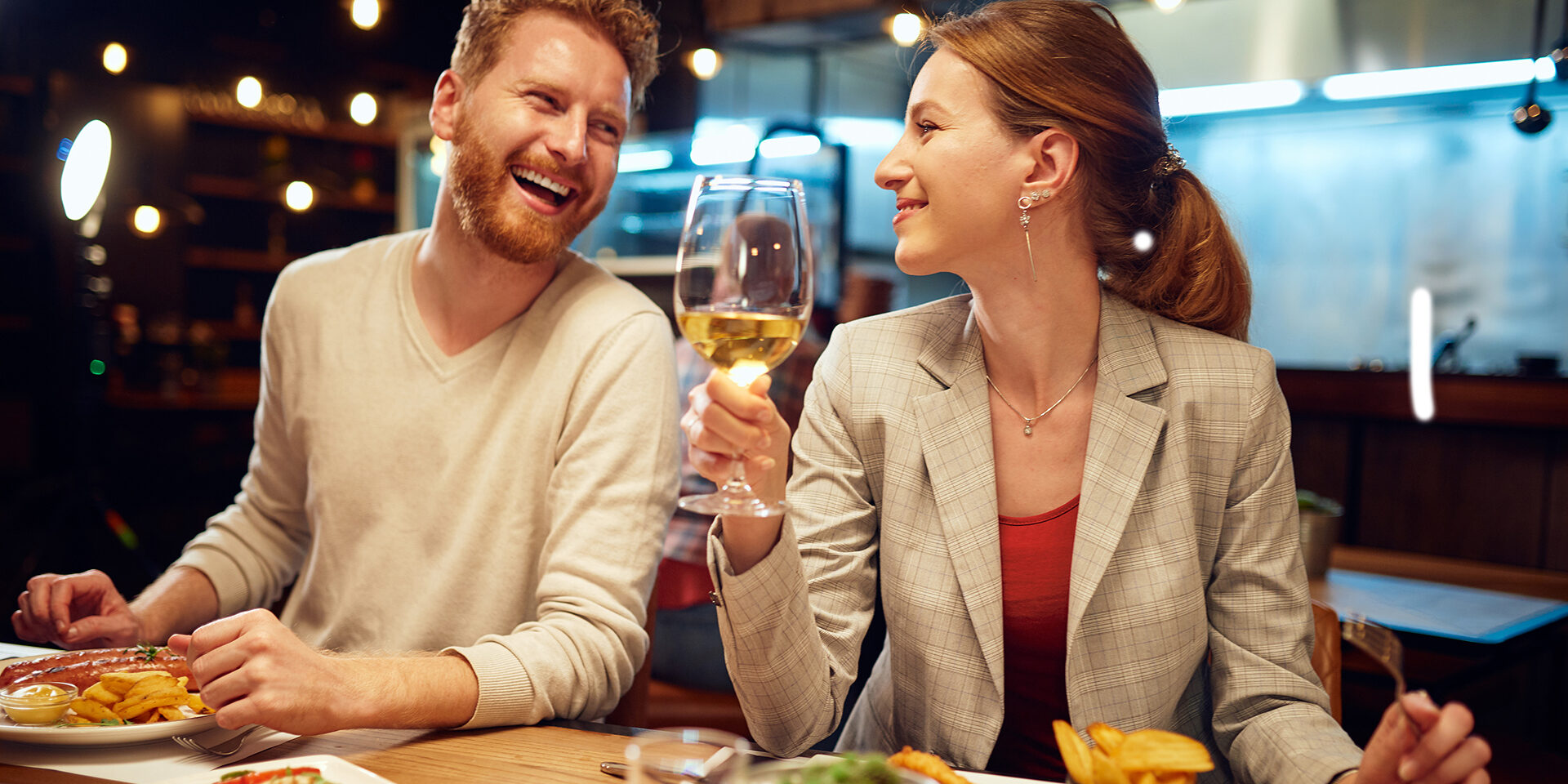Smiling cheerful couple sitting in a restaurant, having dinner and chatting. Man talking to a woman while a woman listening to him and drinking white wine.