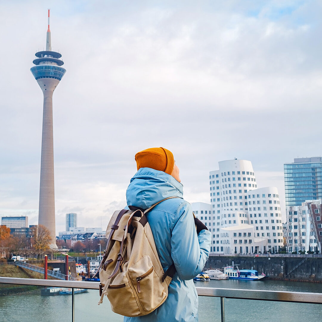 autumn or winter travel to Dusseldorf, Germany. young Asian tourist or student in blue jacket and yellow hat ( symbol of Ukraine) walks through sights of European city. beautiful view in the Media Bay