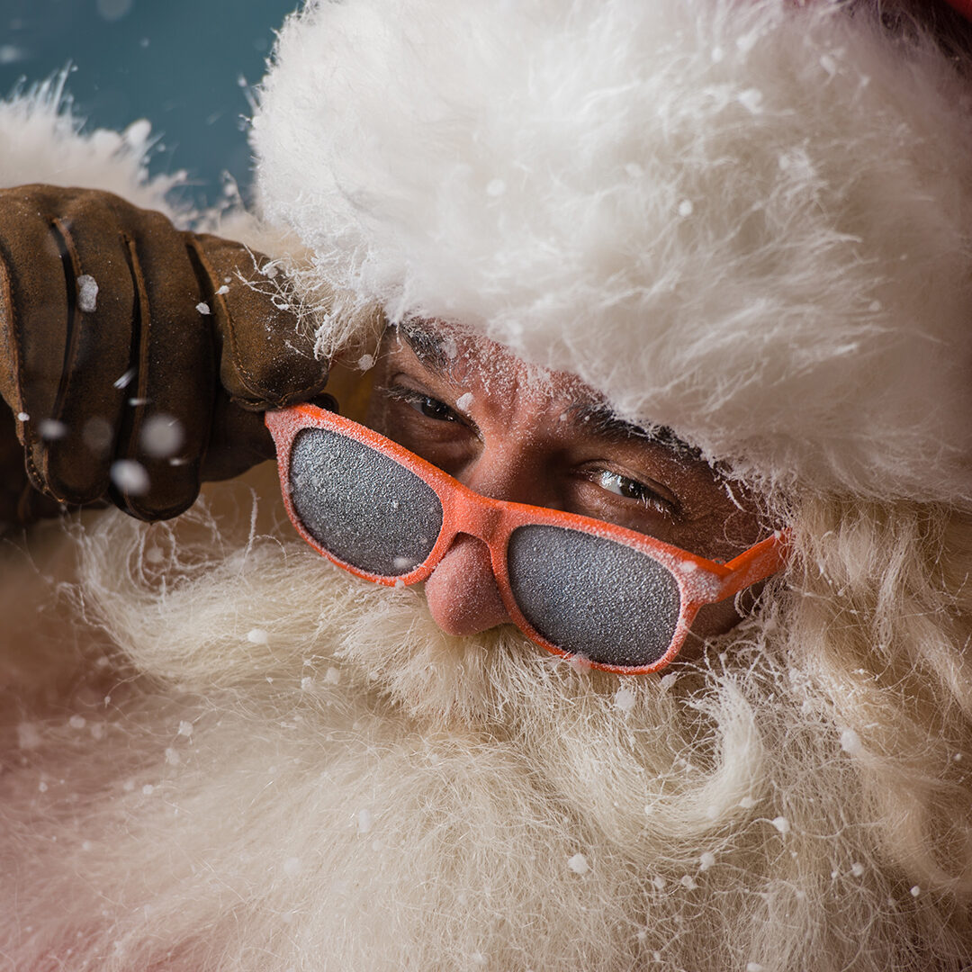 Santa Claus wearing sunglasses dancing outdoors at North Pole in snowfall. He is celebrating Christmas after hard work