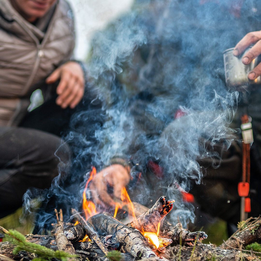 Low angle view of an unrecognizable man and woman camping in the forest preparing tea on a campfire.