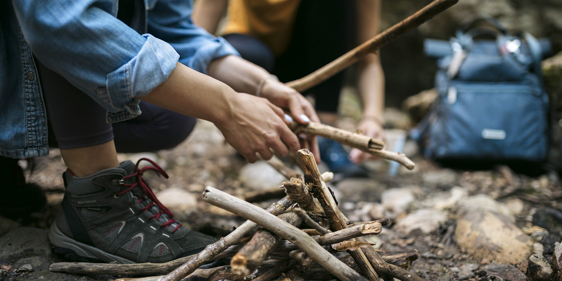 Cropped shot of women hikers preparing campfire on forest trail Close-up of two female hikers arranging sticks for campfire together for cooking food. Cropped shot of women hikers preparing campfire on forest trail.