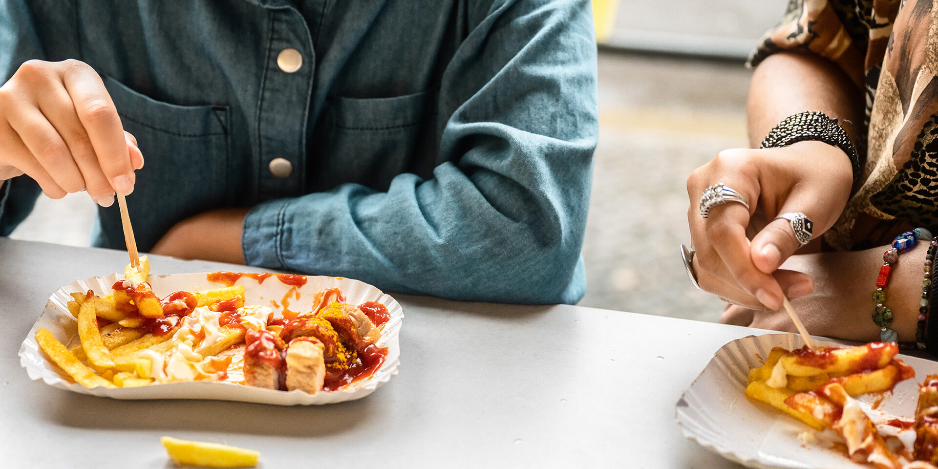 two female hands eating curry sausage with french fries close up of two female hands eating curry sausage with french fries outdoors at table