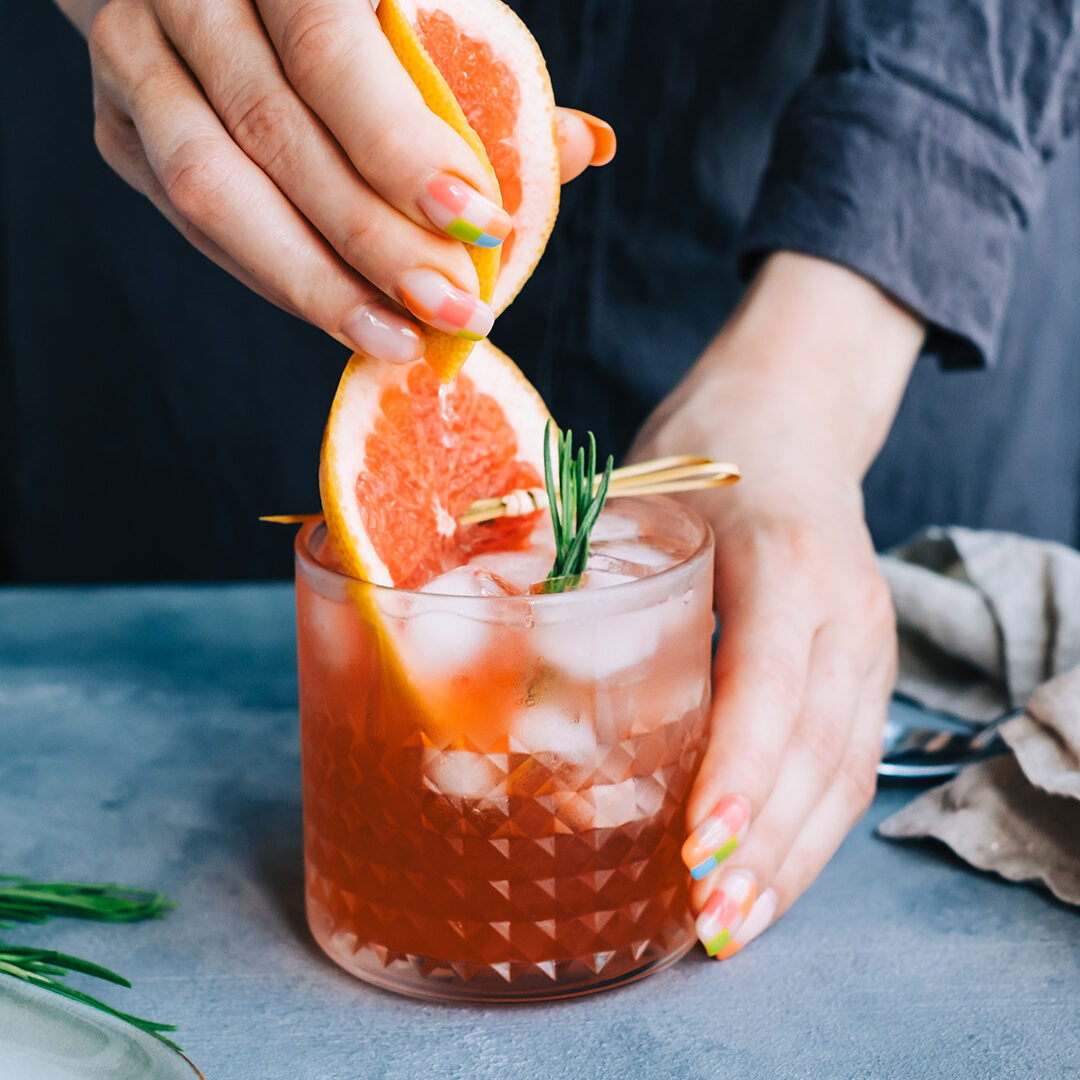 Female bartender hand squeezes juice from fresh grapefruitÂ in cocktail lemonade with ice and rosemary.