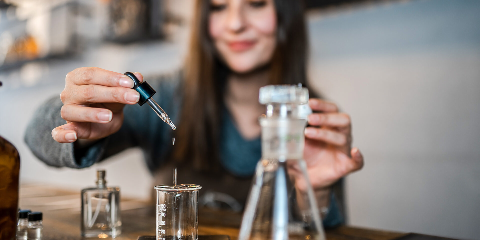Young Perfumer preparing perfume while sitting at table in her own store Young Perfumer preparing perfume while sitting at table in her own store