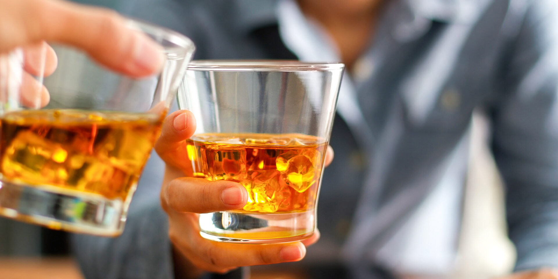 Close-up two men clinking glasses of whiskey drink alcohol beverage together at counter in the pub Close-up two men clinking glasses of whiskey drink alcohol beverage together at counter in the pub