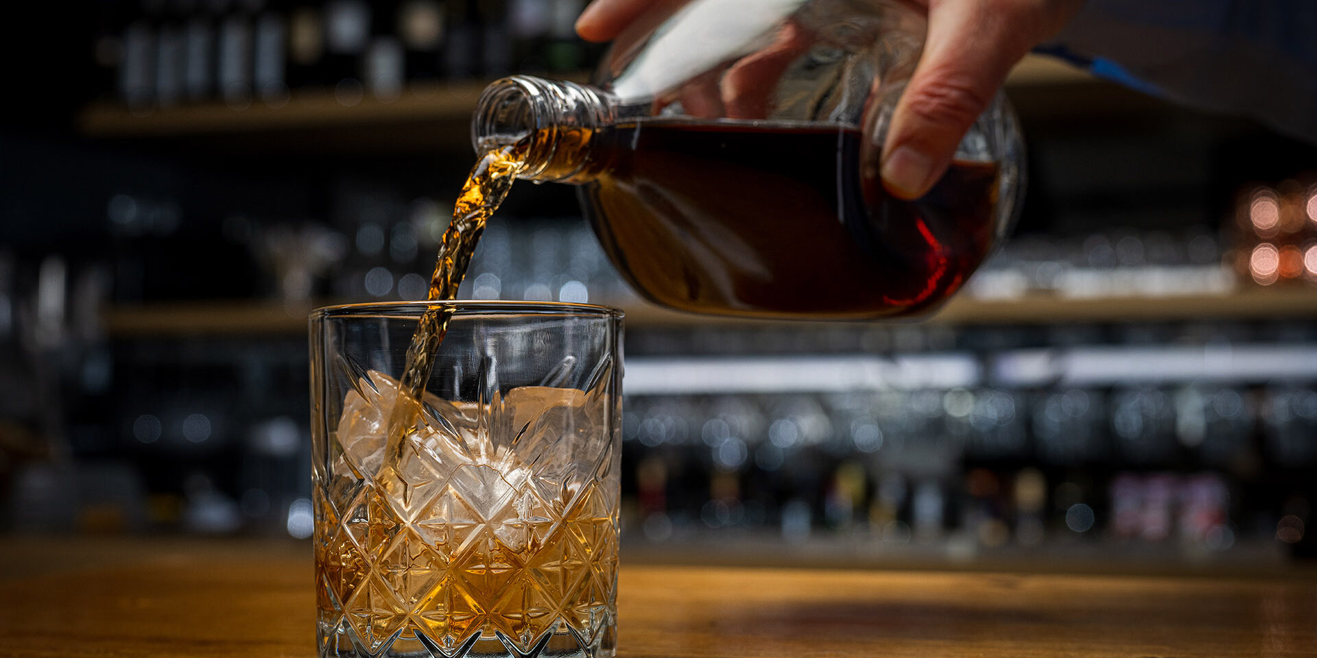 Man preparing drink, pouring old scotch whiskey into glass standing on wooden table. Man preparing drink, pouring old scotch whiskey into glass standing on wooden table. Alcoholic drinks in bar, celebration party and nightlife concept.