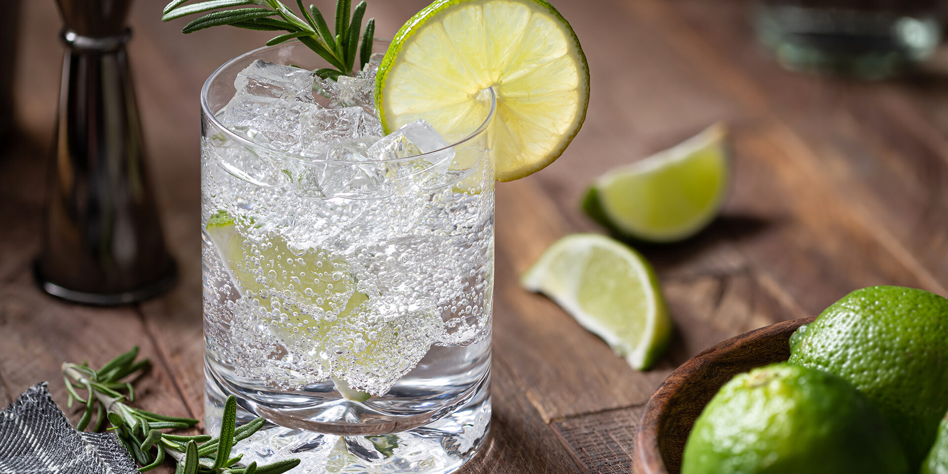 Gin and tonic cocktail with lime. rosemary and ice Gin and tonic cocktail with lime slices, rosemary and ice on a rustic wooden table