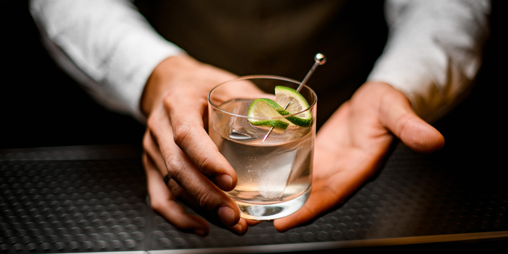 close-up on hands of man bartender holding glass with cold drink beautiful close-up on hands of man bartender holding glass with cold drink with ice cube decorated with lime