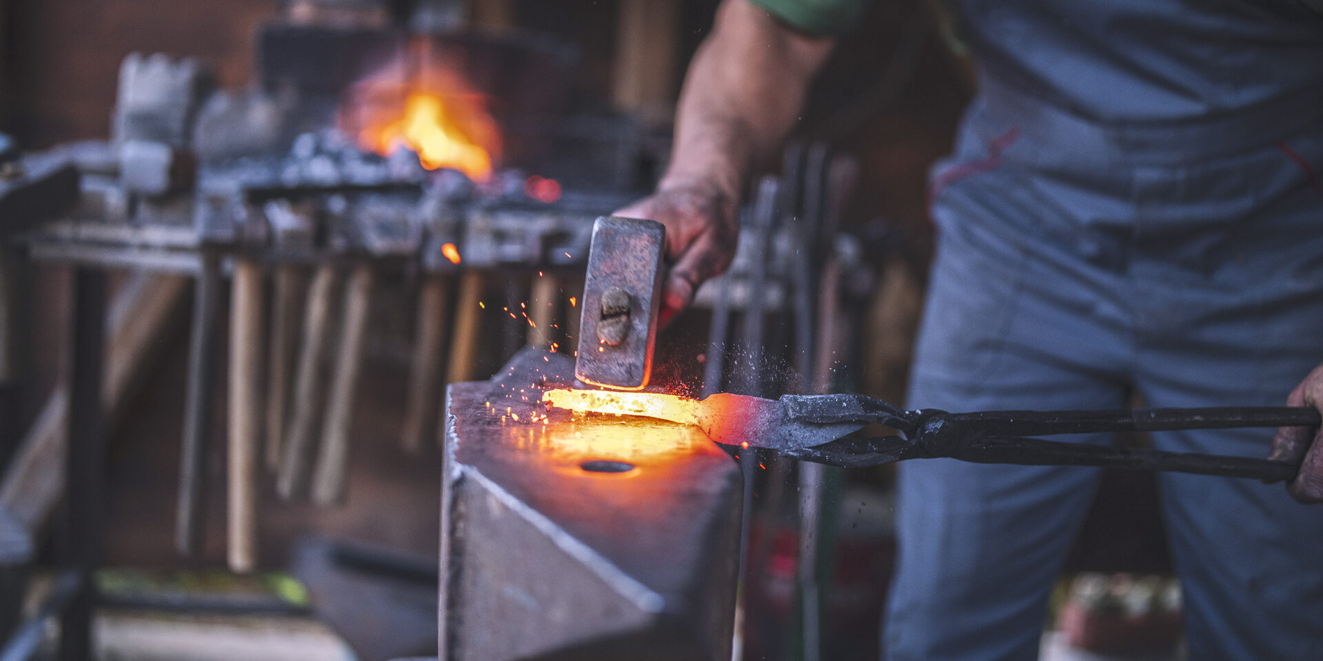 An unrecognizable blacksmith forges hot metal with a hammer on an anvile.