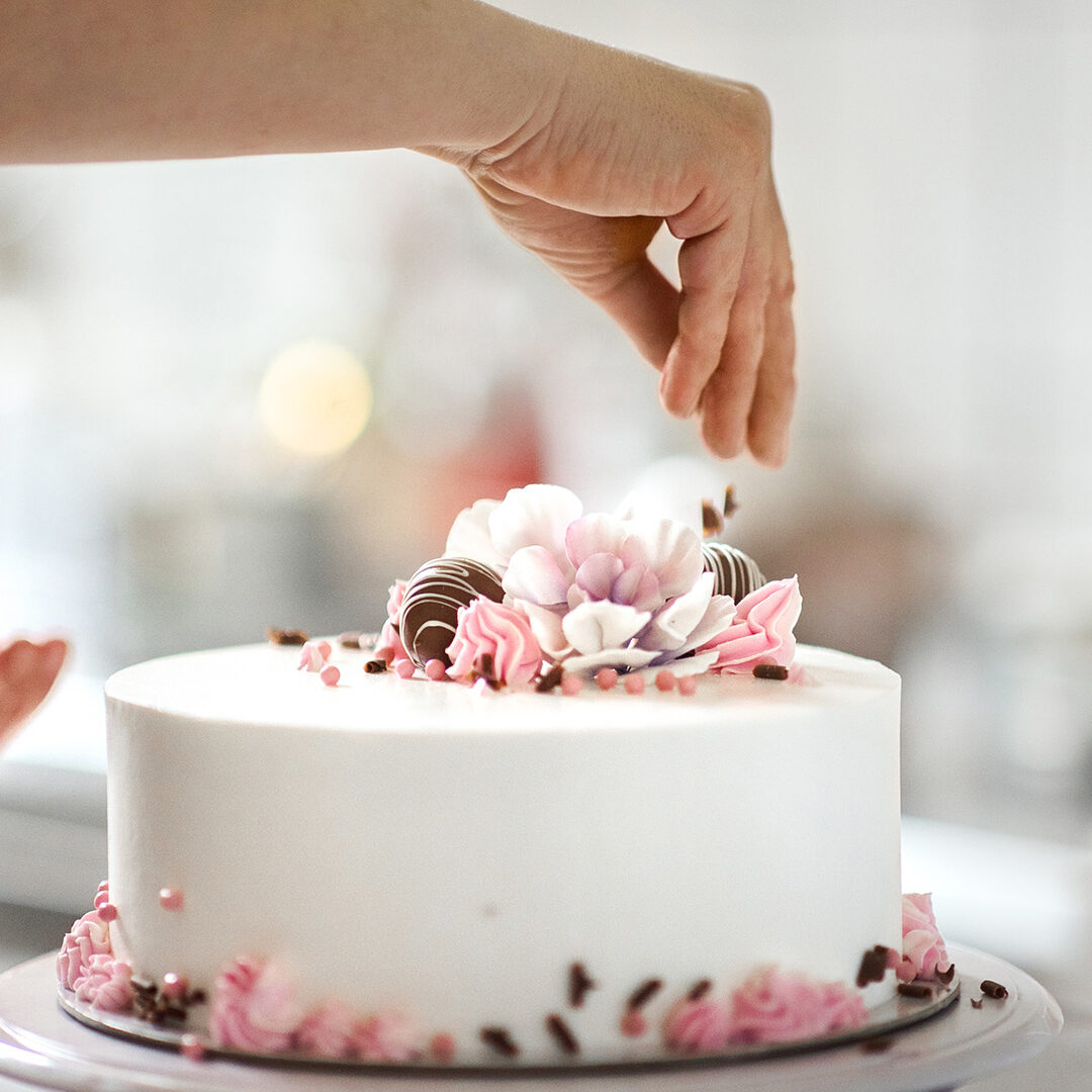 Closeup of an unrecognizable woman decorating a cake at a small family owned cake shop.