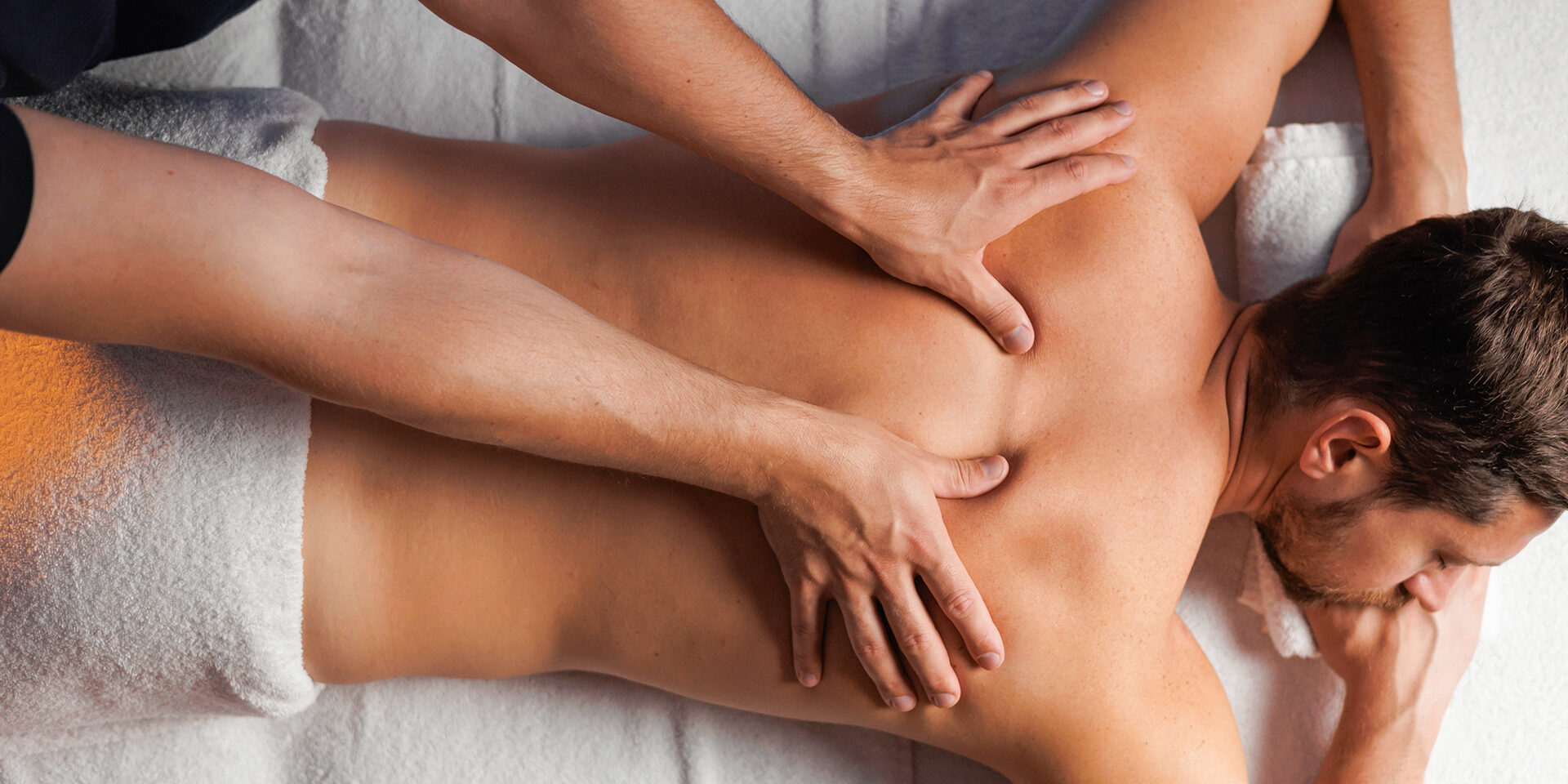 Male masseur massaging the back and shoulders of a man lying on a massage table in a relaxing atmosphere in a spa salon. Therapeutic restorative body massage after office work, health concept. Male masseur massaging the back and shoulders of a man lying on a massage table in a relaxing atmosphere in a spa salon. Therapeutic restorative body massage after office work, health concept
