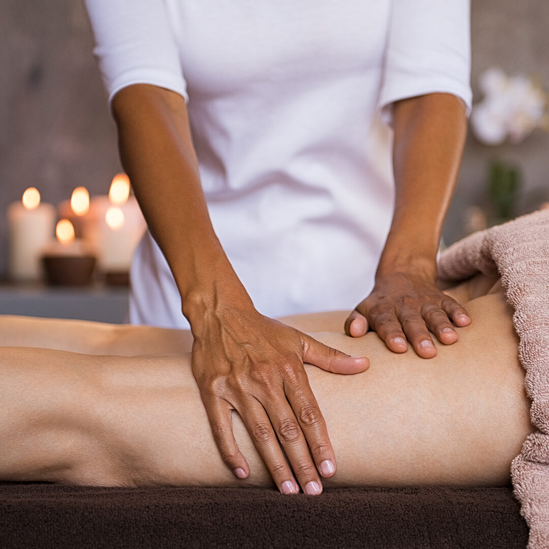 Therapeutic massage for senior woman by beautician at spa salon. Closeup of professional masseuse hands massaging woman legs at wellness center. Anti cellulite treatment and leg drainage on mature woman.