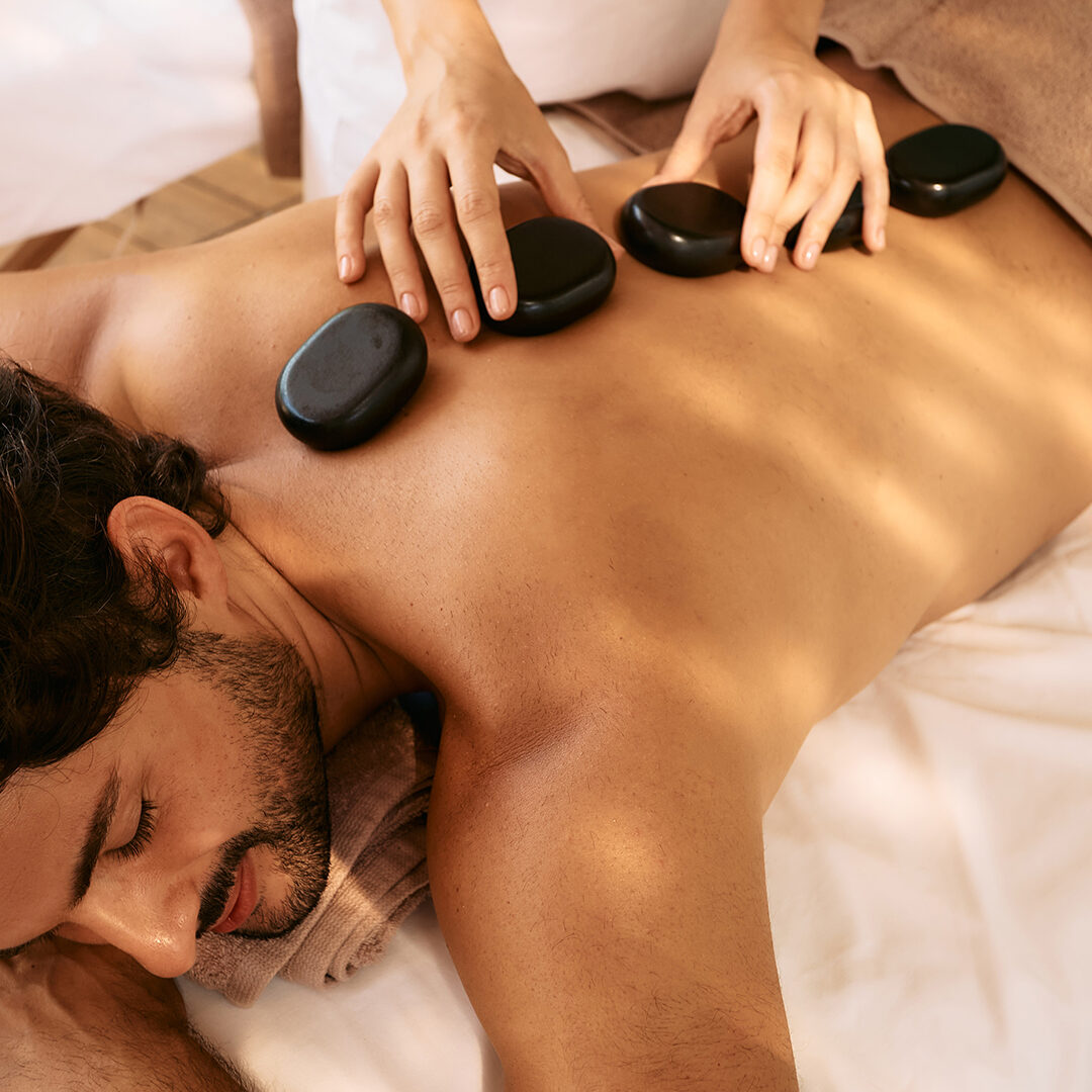 Handsome man at spa resort receives hot stone massage. Hot stone massage therapy using smooth, flat, heated stones