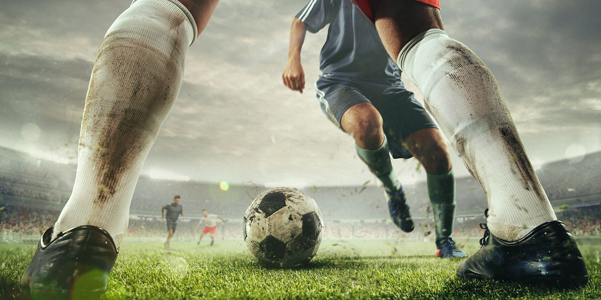 Close up legs of football or soccer players during football match at a stadium filled with spectators, fans. Moment of attacking. Concept of sport, competition, winning, action, motion, overcoming.