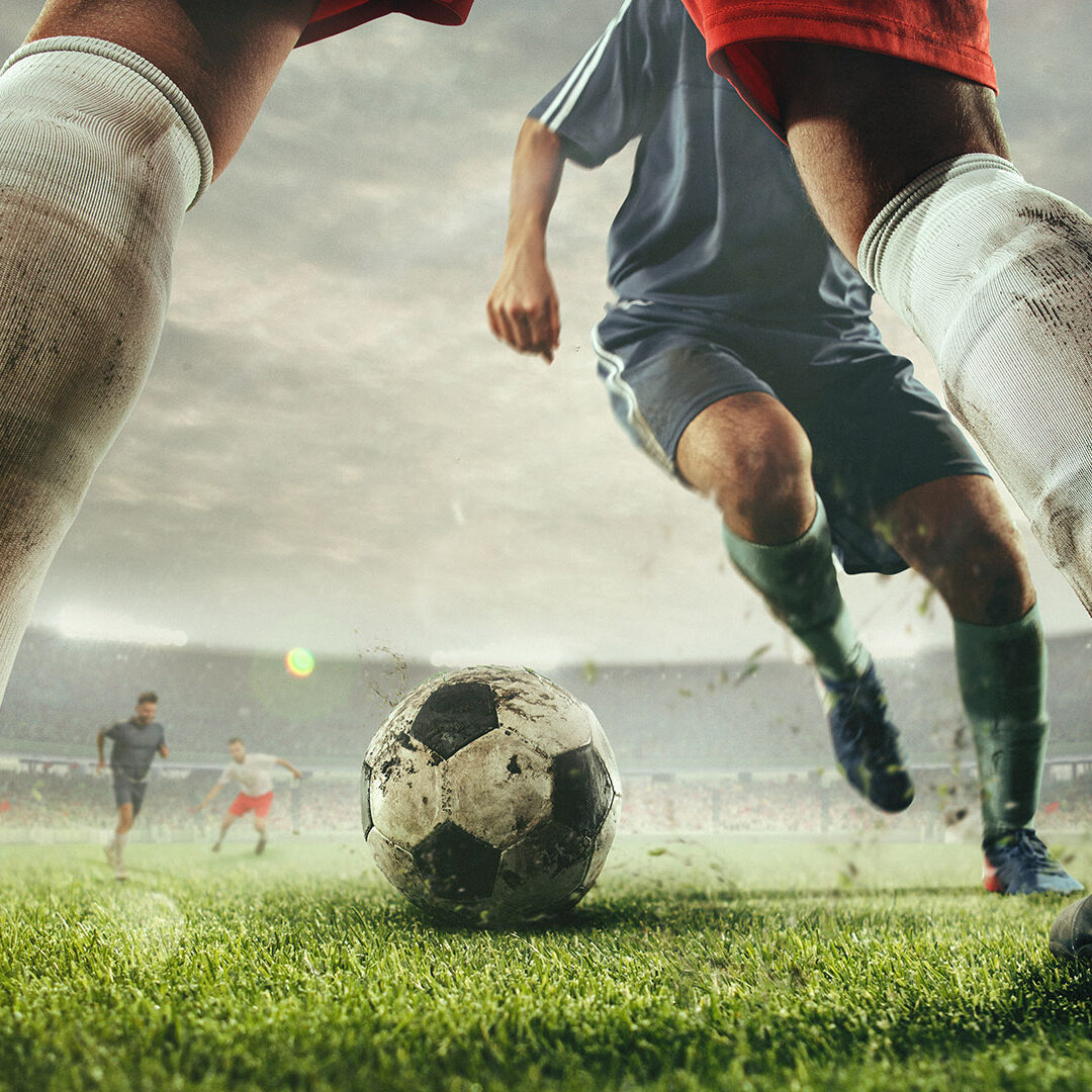 Close up legs of football or soccer players during football match at a stadium filled with spectators, fans. Moment of attacking. Concept of sport, competition, winning, action, motion, overcoming.