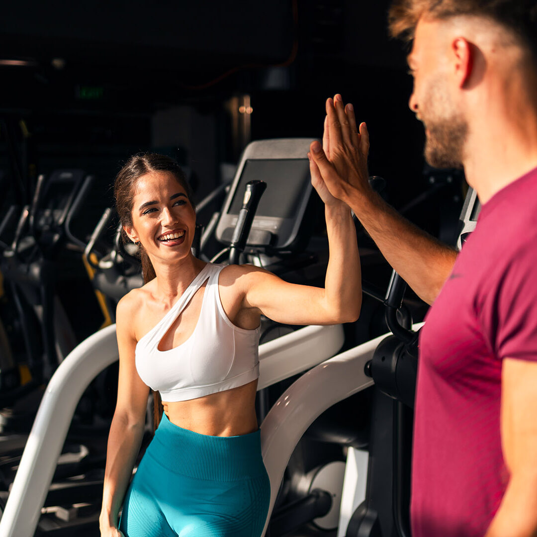 A happy sporty young adult couple giving each other a high five and preparing for a work out session at the gym.