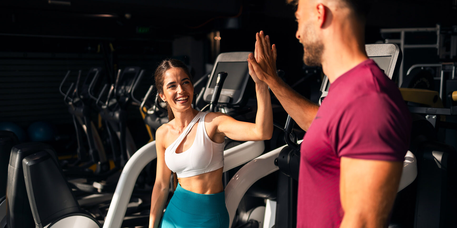 A happy sporty young adult couple giving each other a high five and preparing for a work out session at the gym.