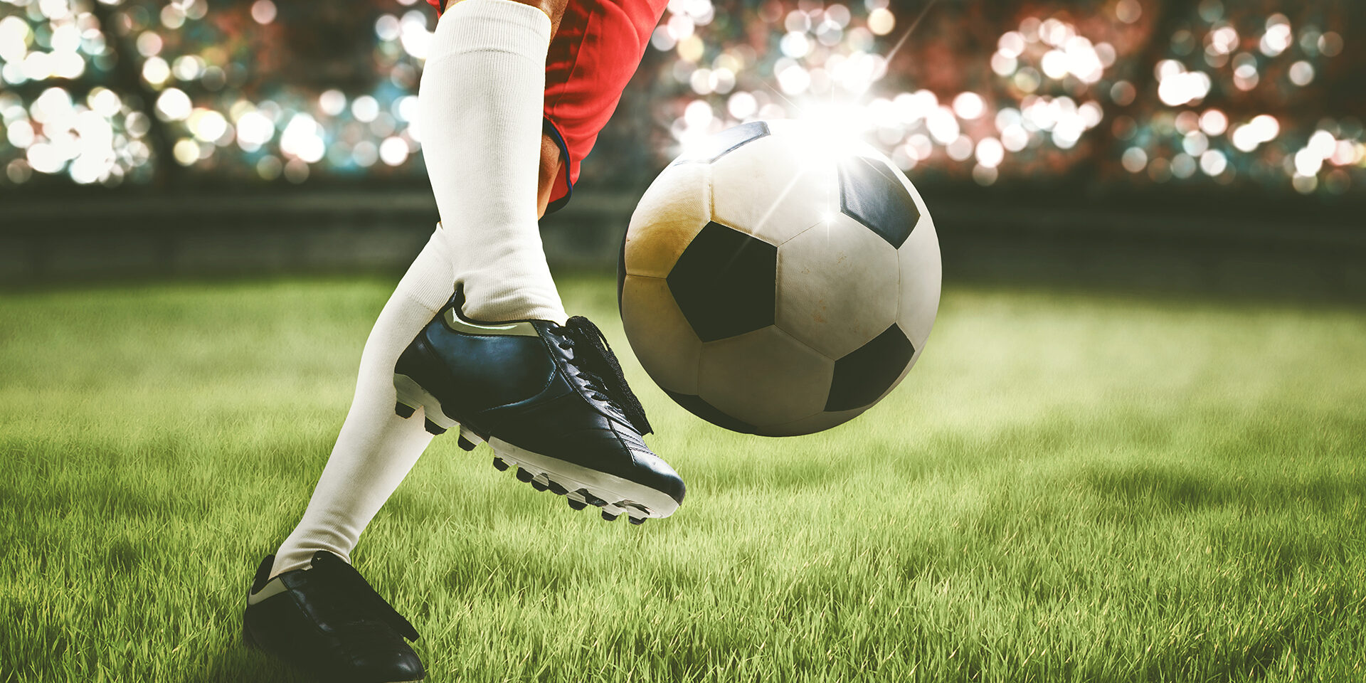 Close up of soccer player feet shooting a ball with powerful toward a goal while playing on a stadium with crowds spectators background