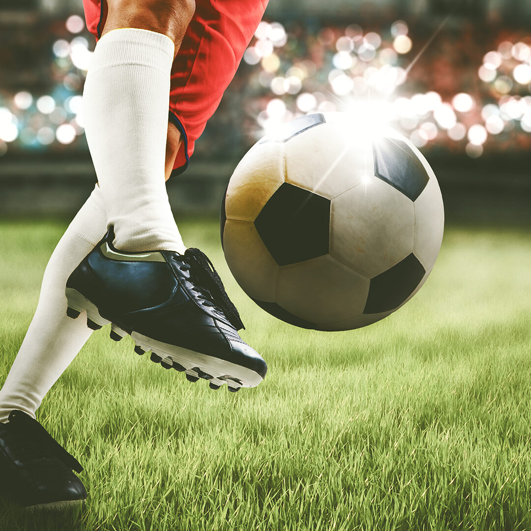 Close up of soccer player feet shooting a ball with powerful toward a goal while playing on a stadium with crowds spectators background