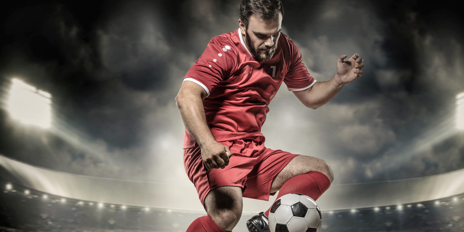 Bearded caucasian Football Player controlling a Soccer Ball in front of Stadium Lights