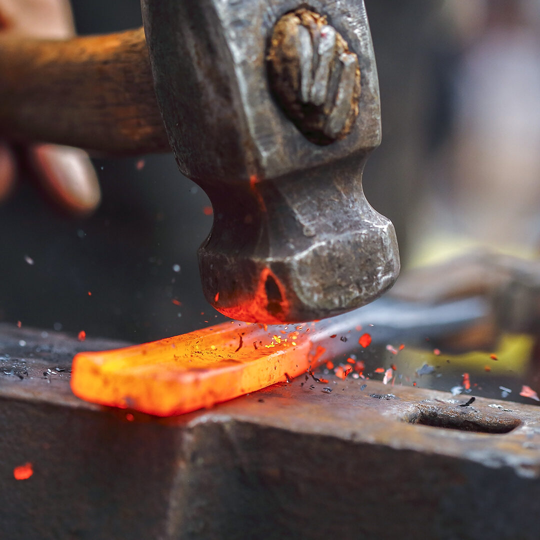 Detail shot of hammer forging hot iron at anvil