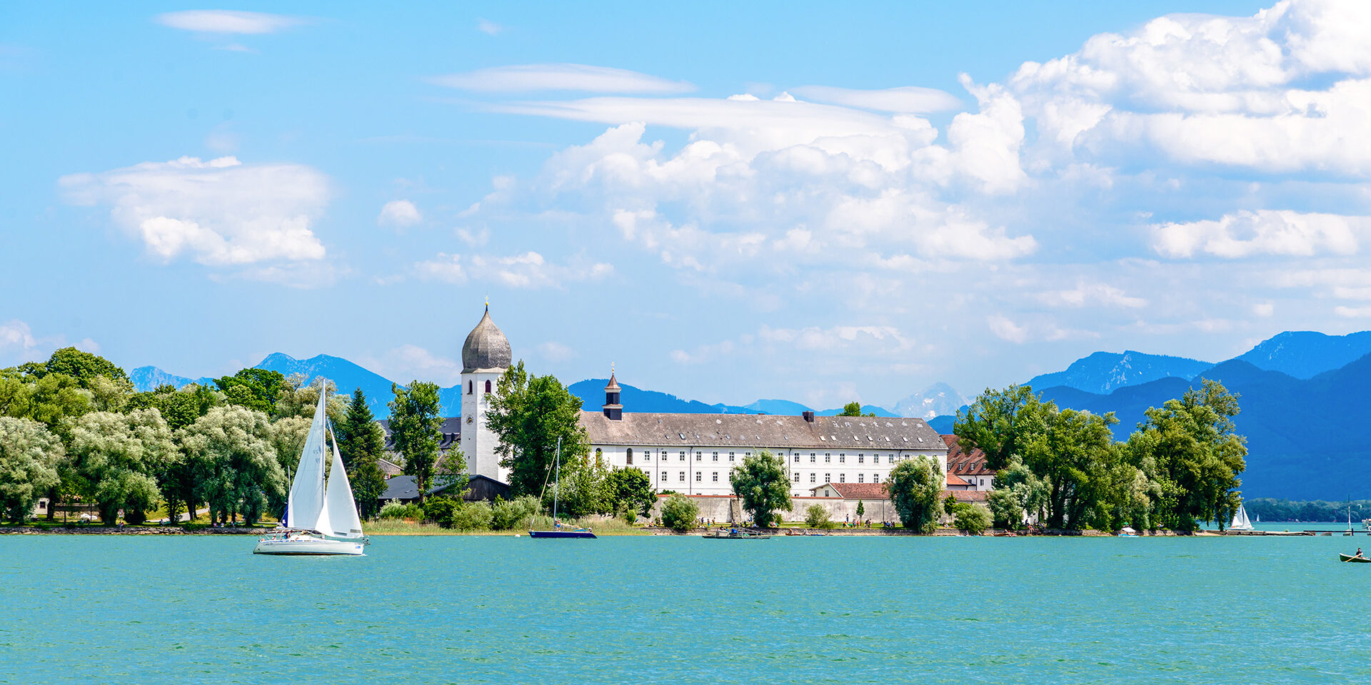 Lake Chiemsee with a boat, sailboat, church, blue sky. clouds. Bavaria, Germany