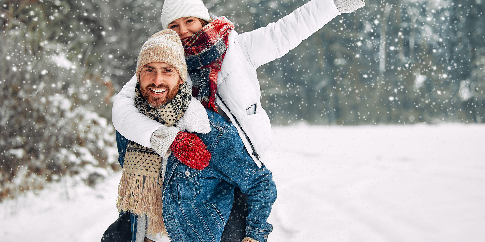 Couple having fun on winter vacation, boyfriend piggybacking girlfriend while spending time outdoor on snowy winter day in mountains.