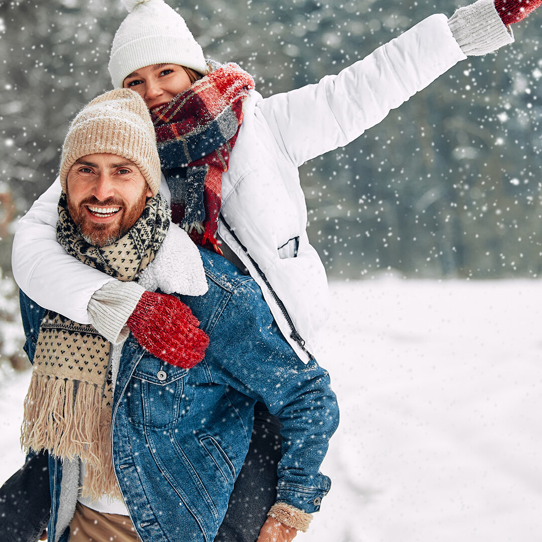 Couple having fun on winter vacation, boyfriend piggybacking girlfriend while spending time outdoor on snowy winter day in mountains.