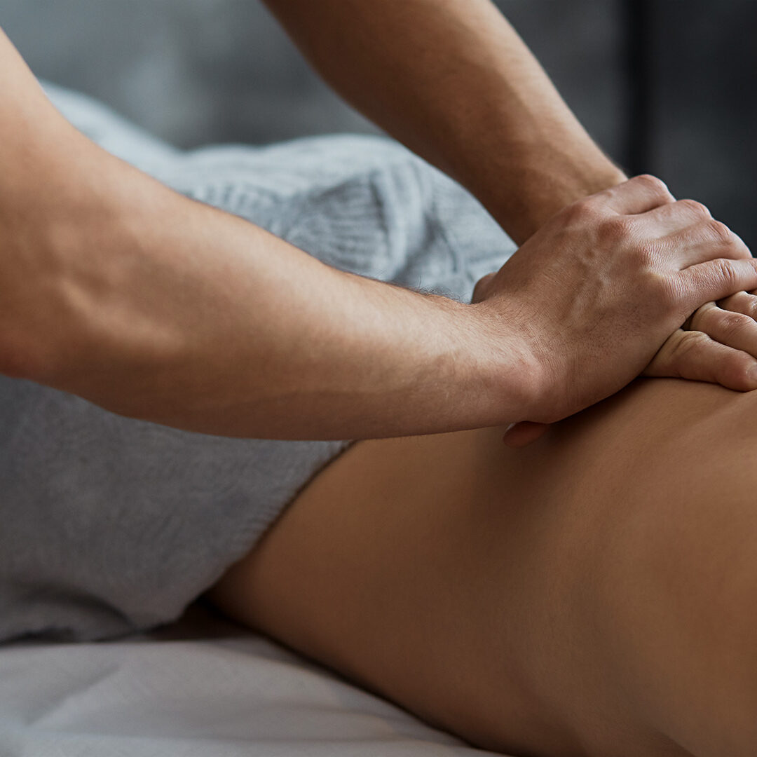 Young handsome man enjoying a back massage. Professional massage therapist is treating a male patient in apartment. Relaxation, beauty, body and face treatment concept. Home massage.