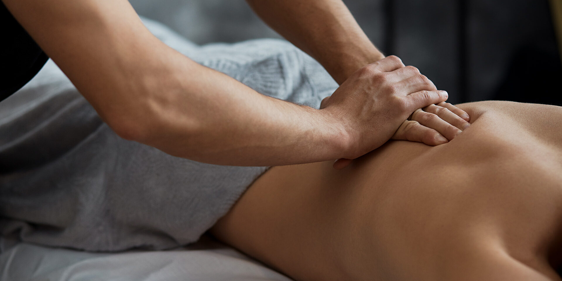 Young handsome man enjoying a back massage. Professional massage therapist is treating a male patient in apartment. Relaxation, beauty, body and face treatment concept. Home massage.