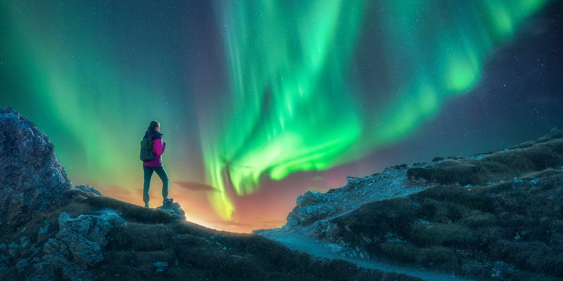 Northern lights and young woman on mountain peak at night. Aurora borealis and silhouette of alone girl on mountain trail. Landscape with polar lights. Starry sky with bright aurora. Travel background