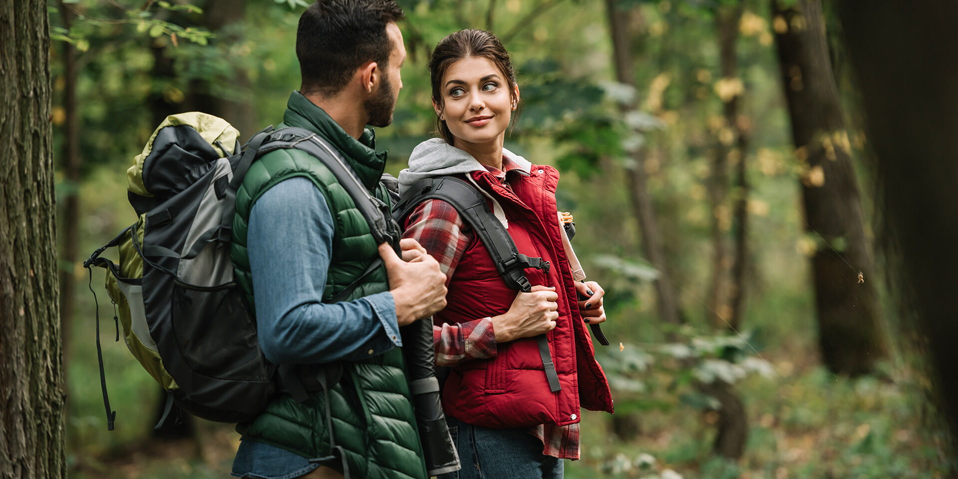 side view of man and woman with backpacks hiking in woods