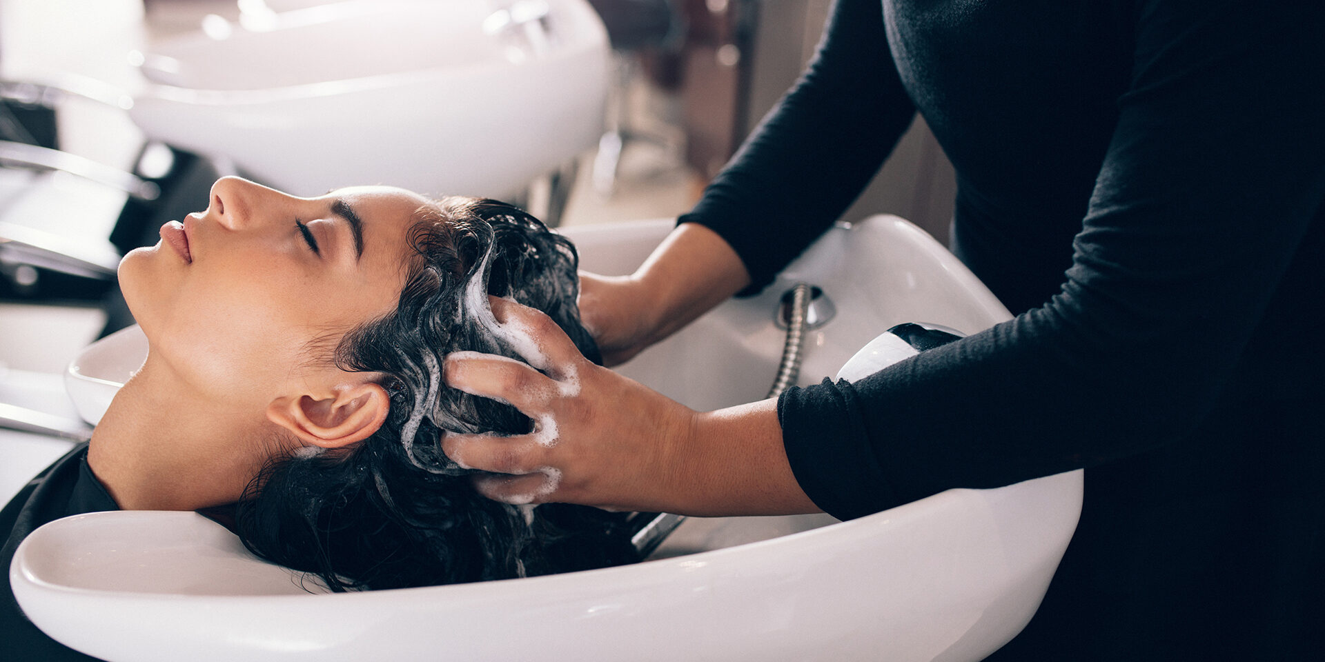 Woman applying shampoo and massaging hair of a customer. Woman having her hair washed in a hairdressing salon.