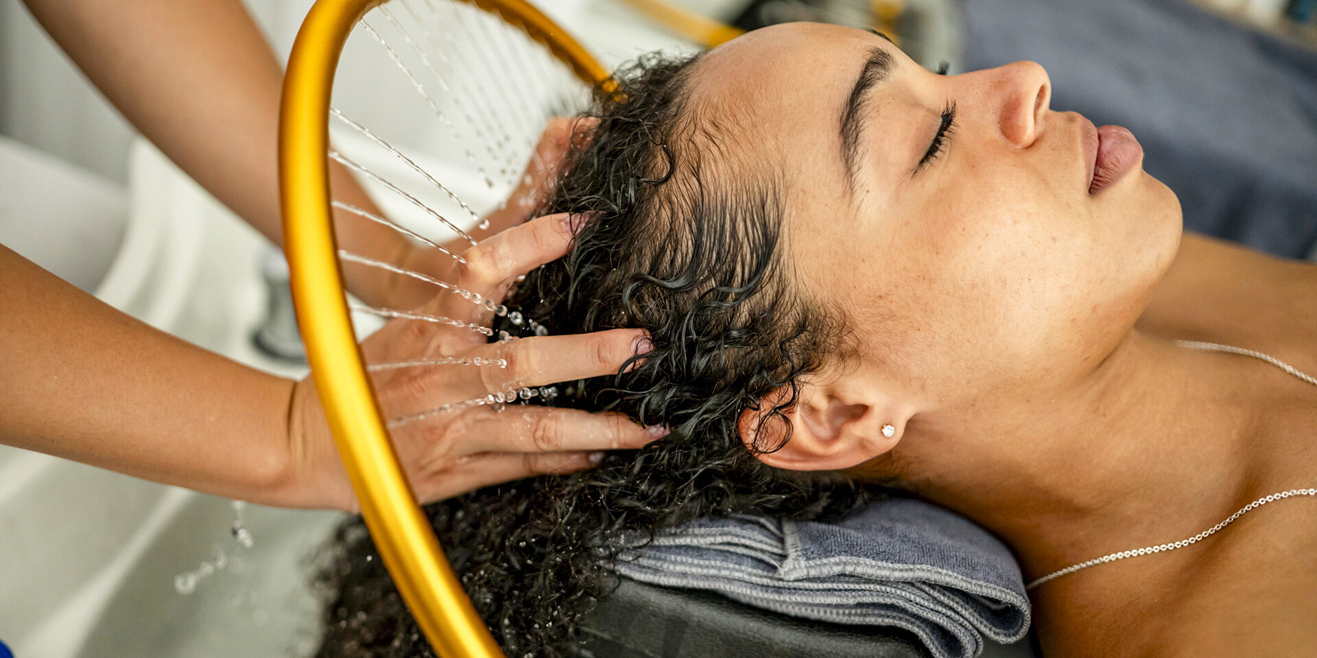 A woman enjoying a relaxing hair wash at a salon. She lies back with closed eyes, enjoying a gentle scalp massage under a stream of warm water.