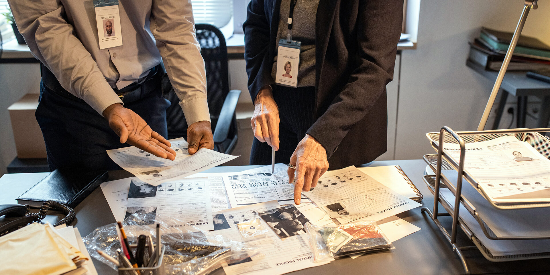 Hands of intercultural agents of FBI discussing criminal profiles by workplace Hands of intercultural agents of FBI discussing criminal profiles by workplace while one of them pointing at photo of suspect