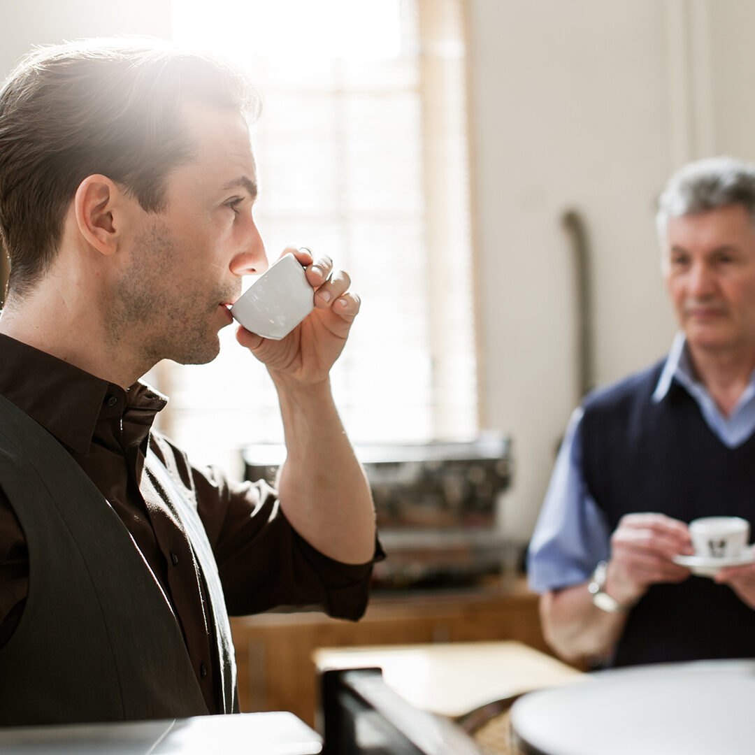 Owner of coffee roaster testing a new coffee blend. The master taster is standing in the background with a cup of the coffee. Horizontal shot.