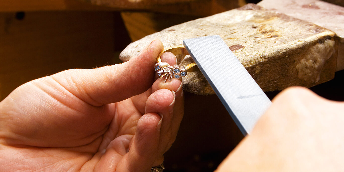 Making a ring. Ring is a setting with no stones being filed. Woman's hands. Focus on ring and fingers.