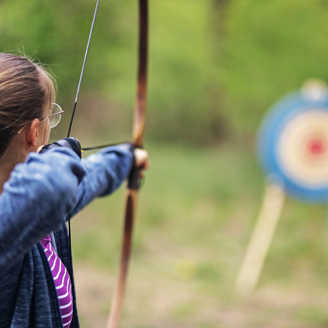 Teenage girl shooting bow outdoors on spring day.
Nikon D850