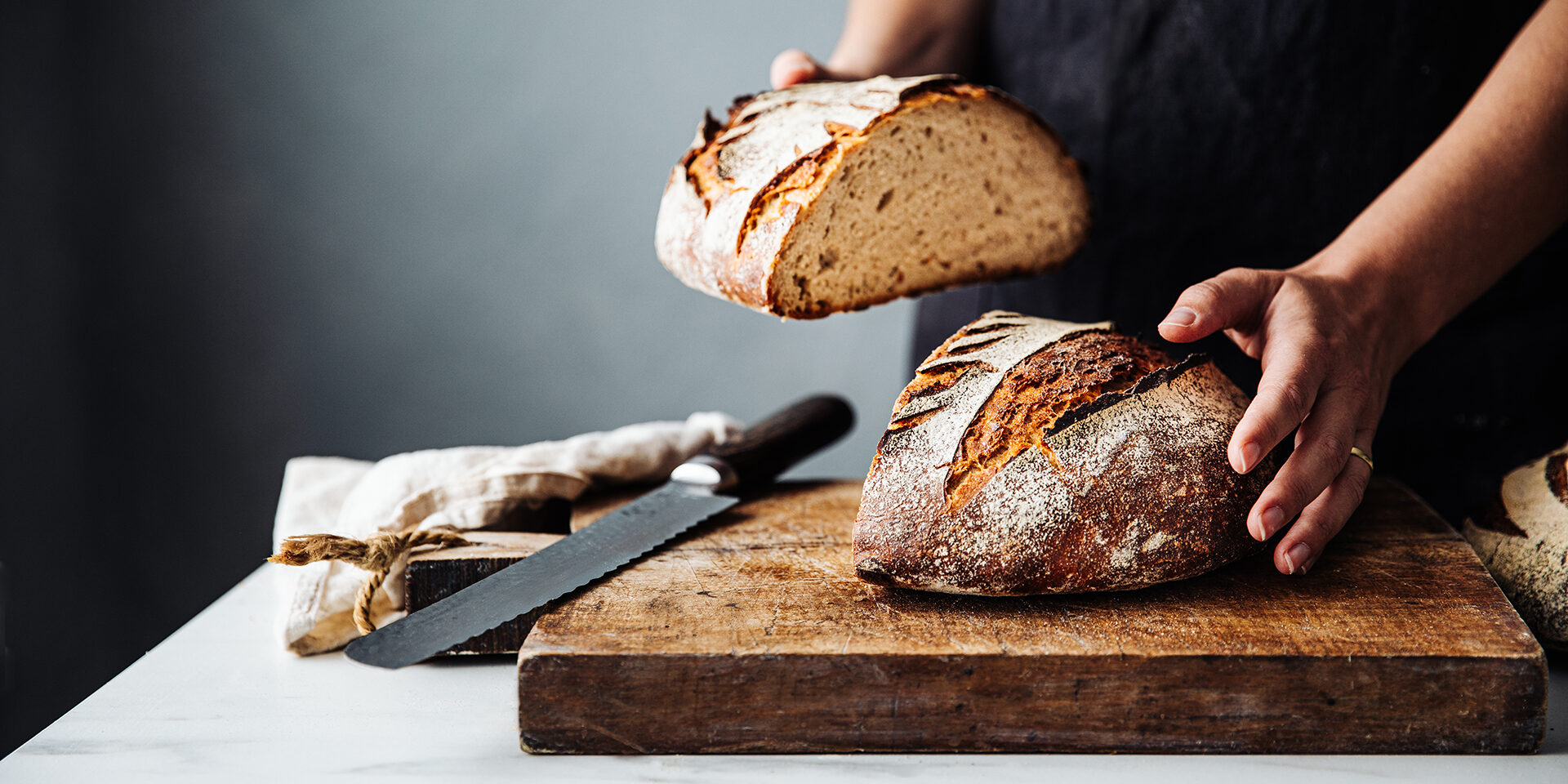 Woman holding bread on cutting board in kitchen Midsection of woman holding bread with knife on cutting board. Close-up of fresh baked sourdough bread at counter. She is in kitchen.