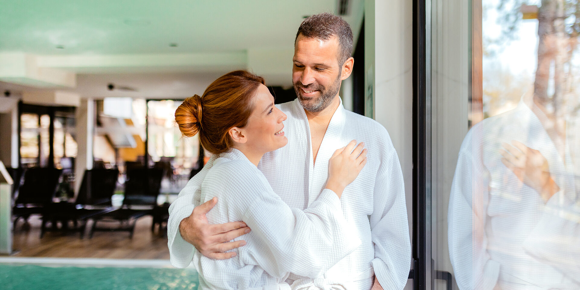 Serene Getaway: Couple Relaxing by the Poolside Window in a Luxury Spa A Couple Wrapped in Soft Bathrobes Stands by the Poolside Window, Admiring Nature in a Serene Spa Setting. A Perfect Visual for Relaxation, Self-care, and Romantic Retreats.